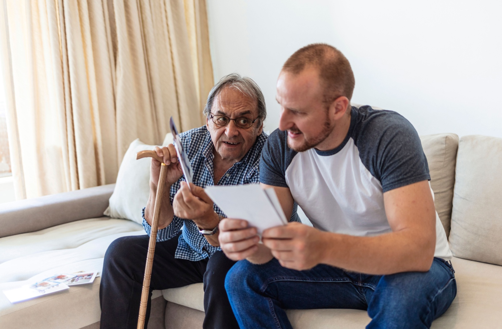 An adult child reminisces over photographs with their senior parent in a memory care community.
