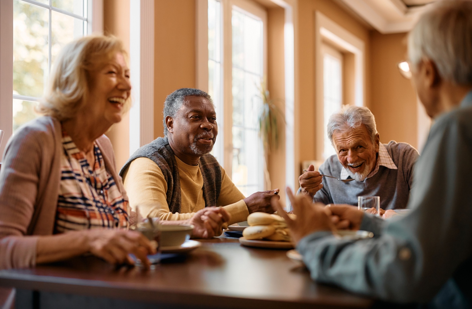 A group of older adults laughing while eating breakfast together in senior living.
