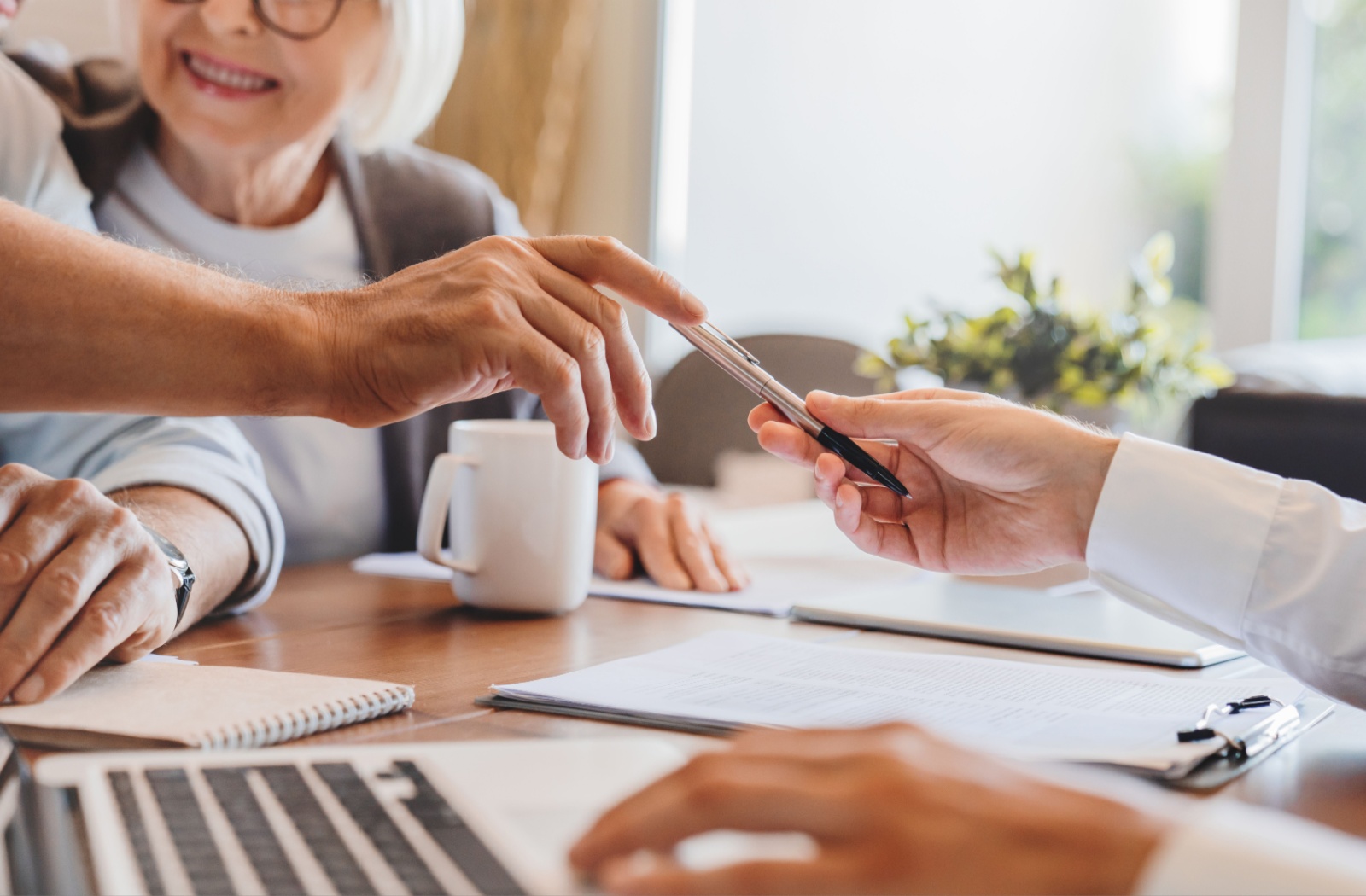 An elder law attorney handing a pen over to an older couple to sign legal documents regarding dementia.