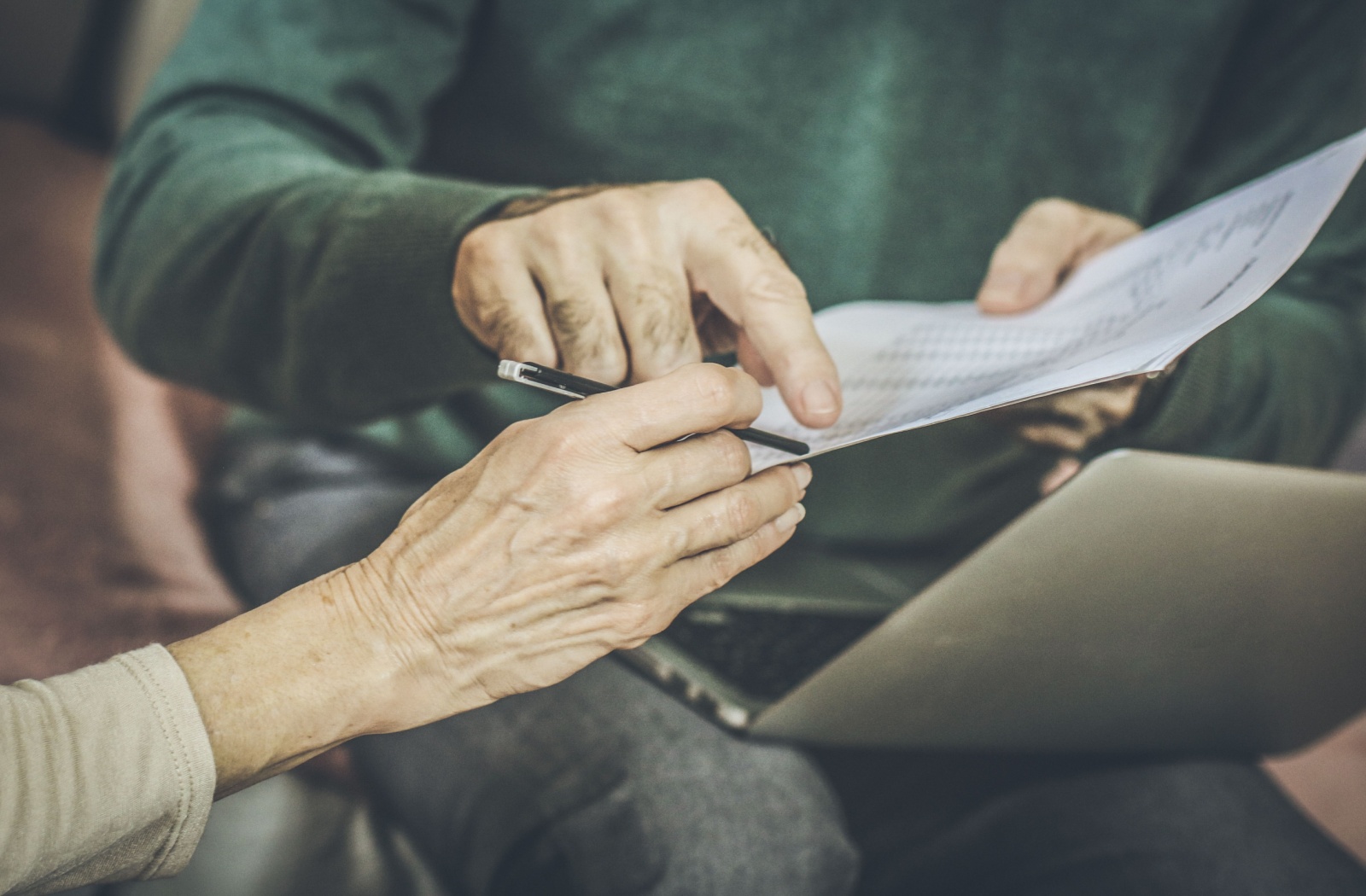 An adult pointing at a piece of paper as an out-of-frame older adult prepares to sign.
