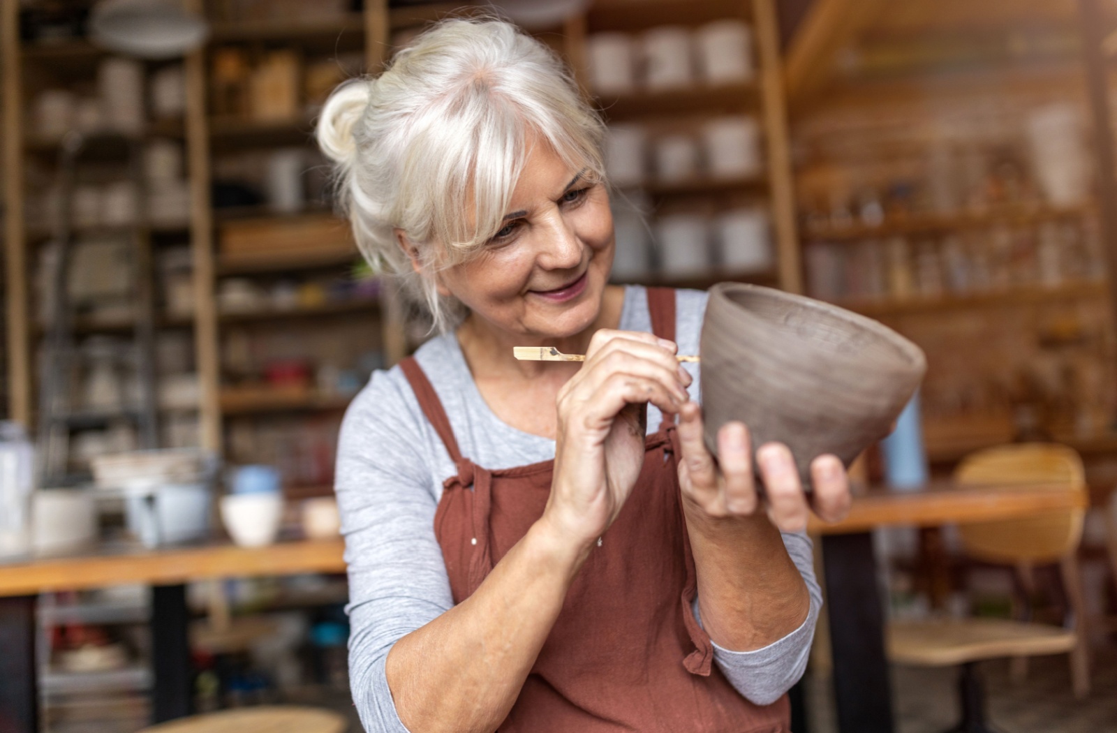 An older adult carefully etching lines into a handcrafted bowl made during a pottery arts and crafts class.