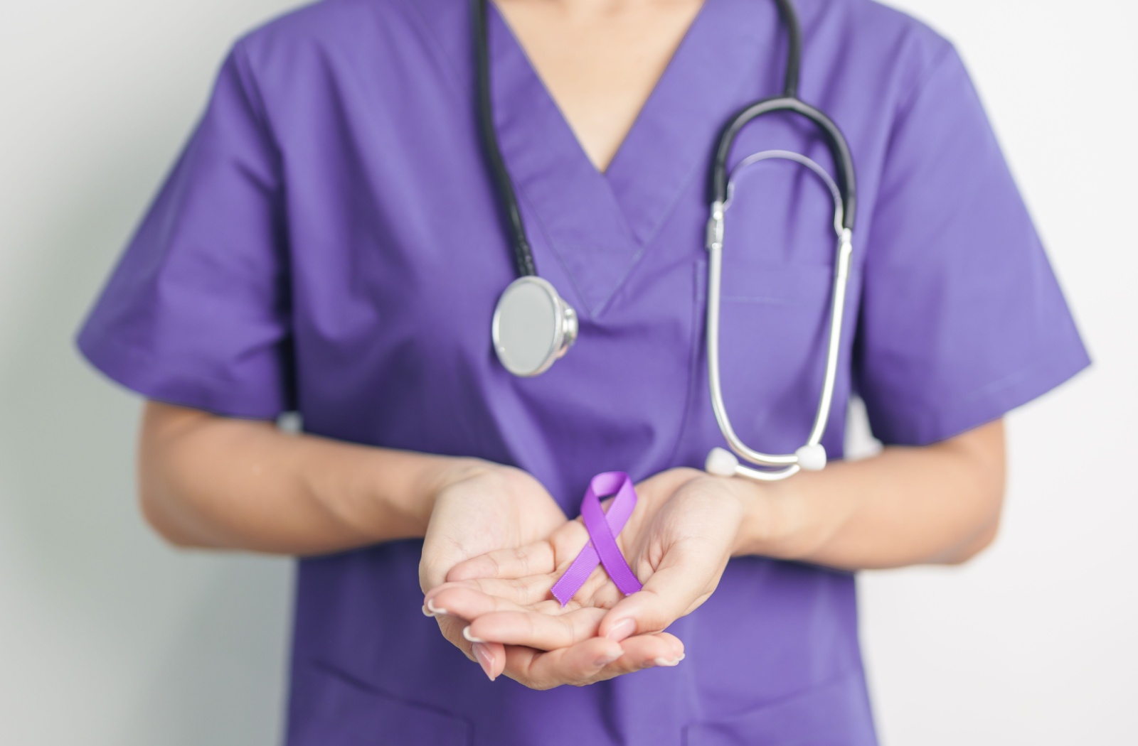 A nurse in purple scrubs holds a purple ribbon in their hands, representing Alzheimer’s awareness and caregiving