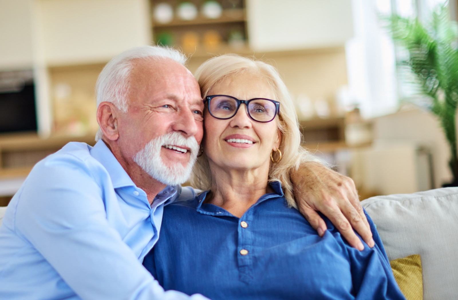 Senior couple sitting together on a couch smiling and embracing in a comfortable assisted living community