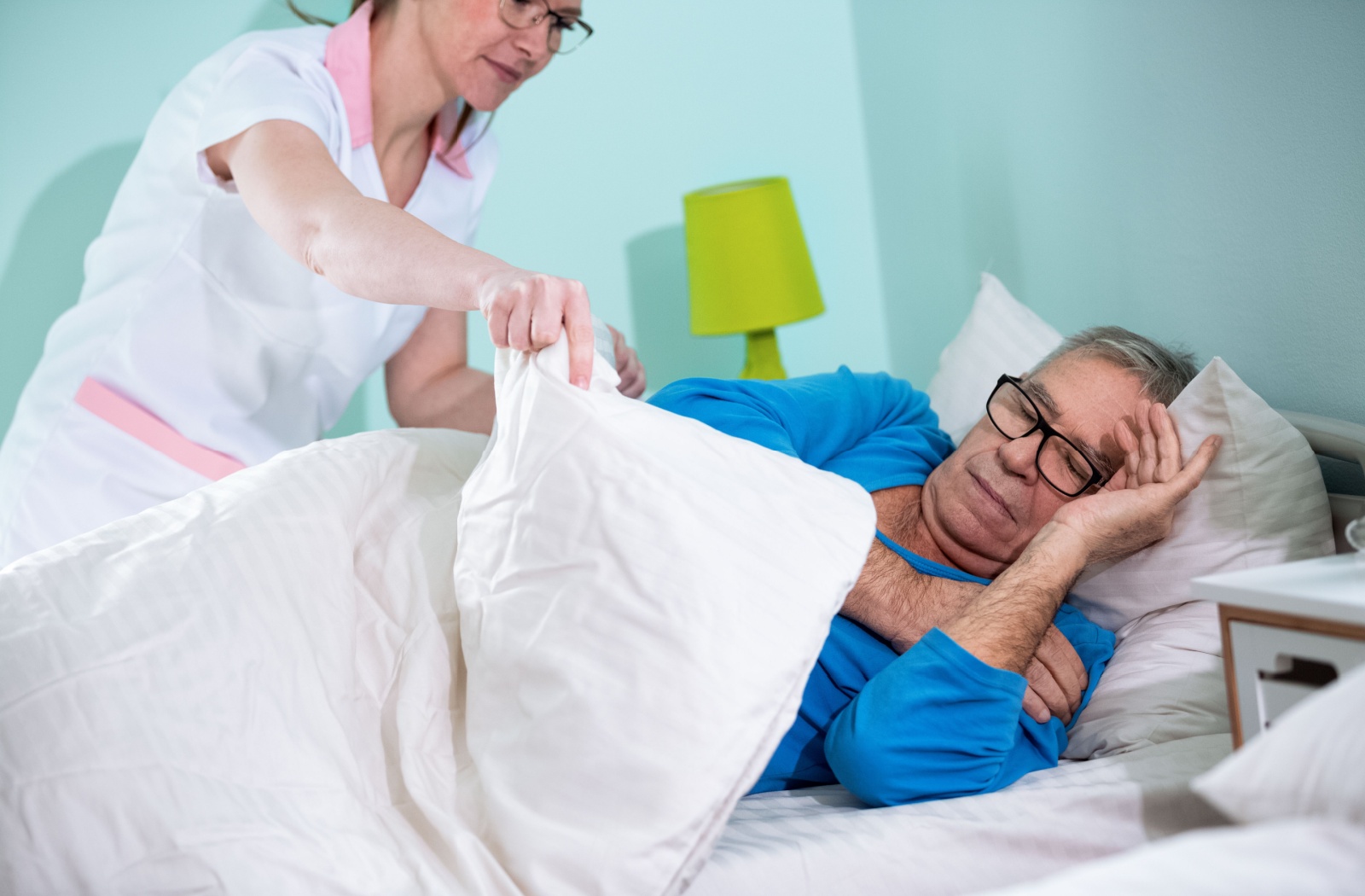 A professional caregiver helping someone with memory loss into bed.
