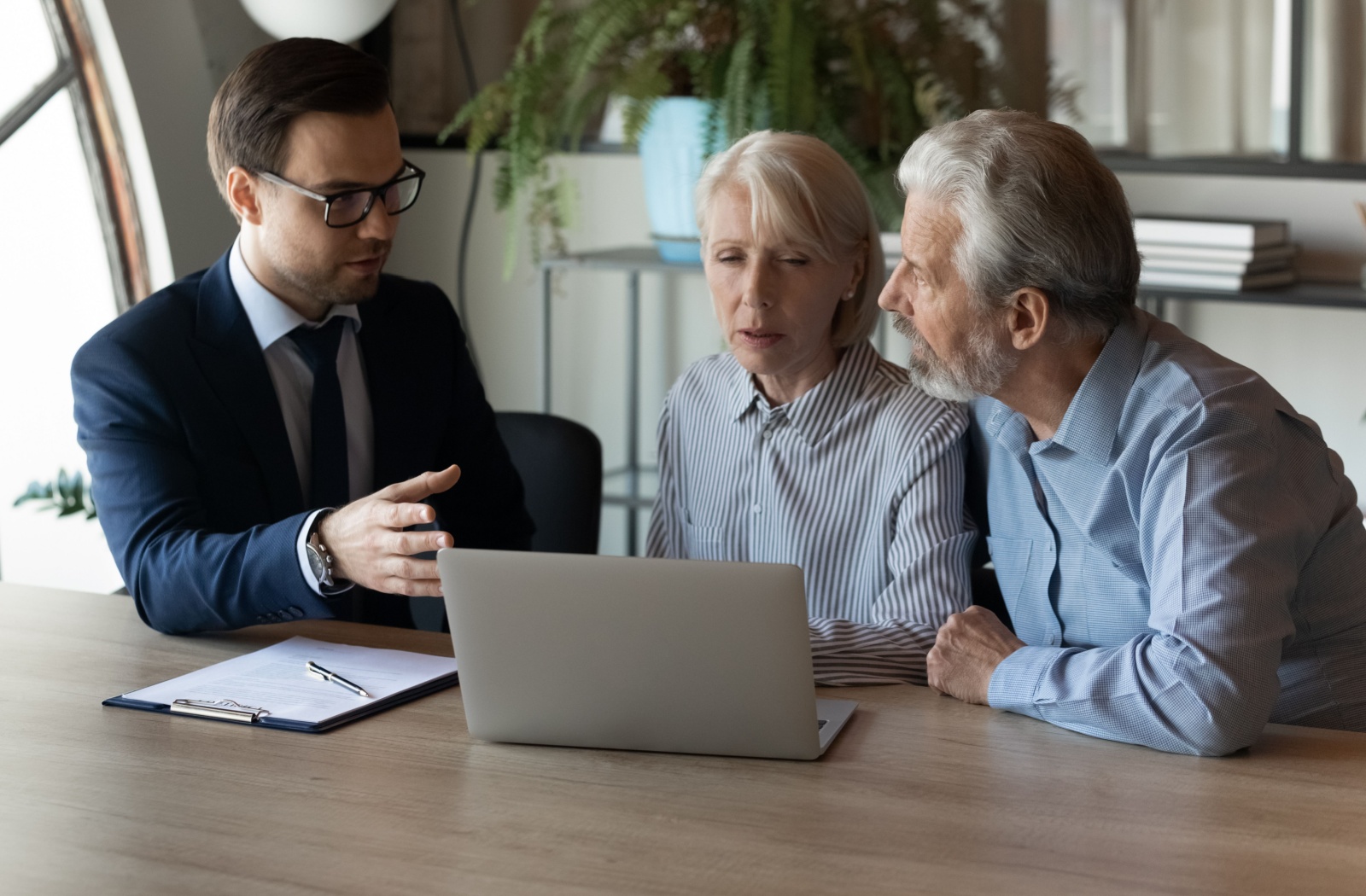 An older adult couple talking to a lawyer in a sunlit office.