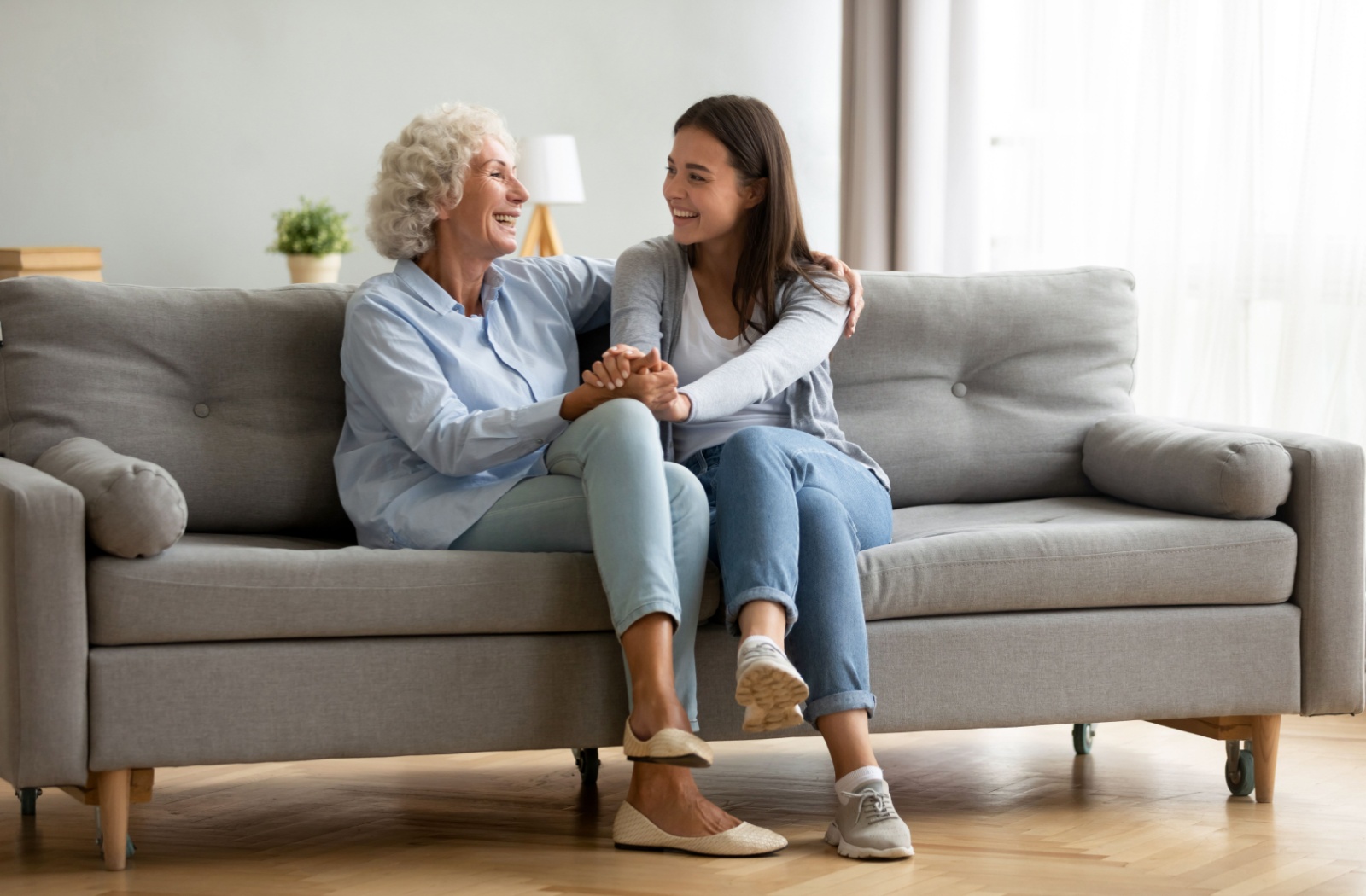 A smiling senior and their adult child embrace each other as they share a happy moment together on the couch.