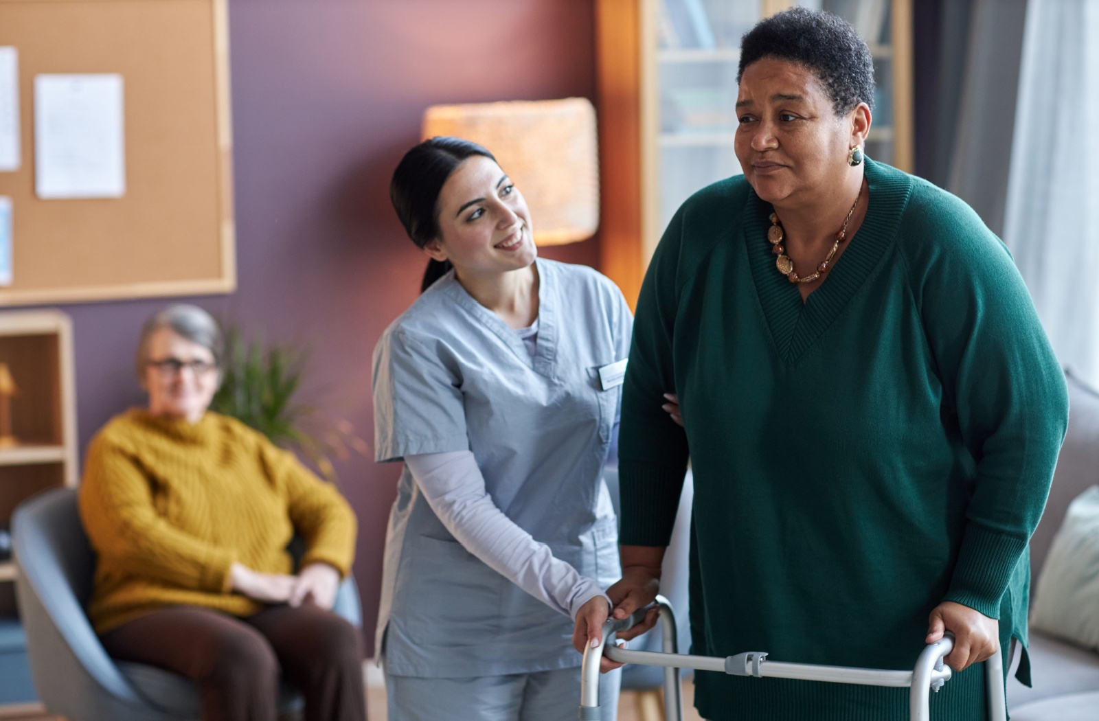 A smiling staff member in assisted living helping an older adult in a walker.