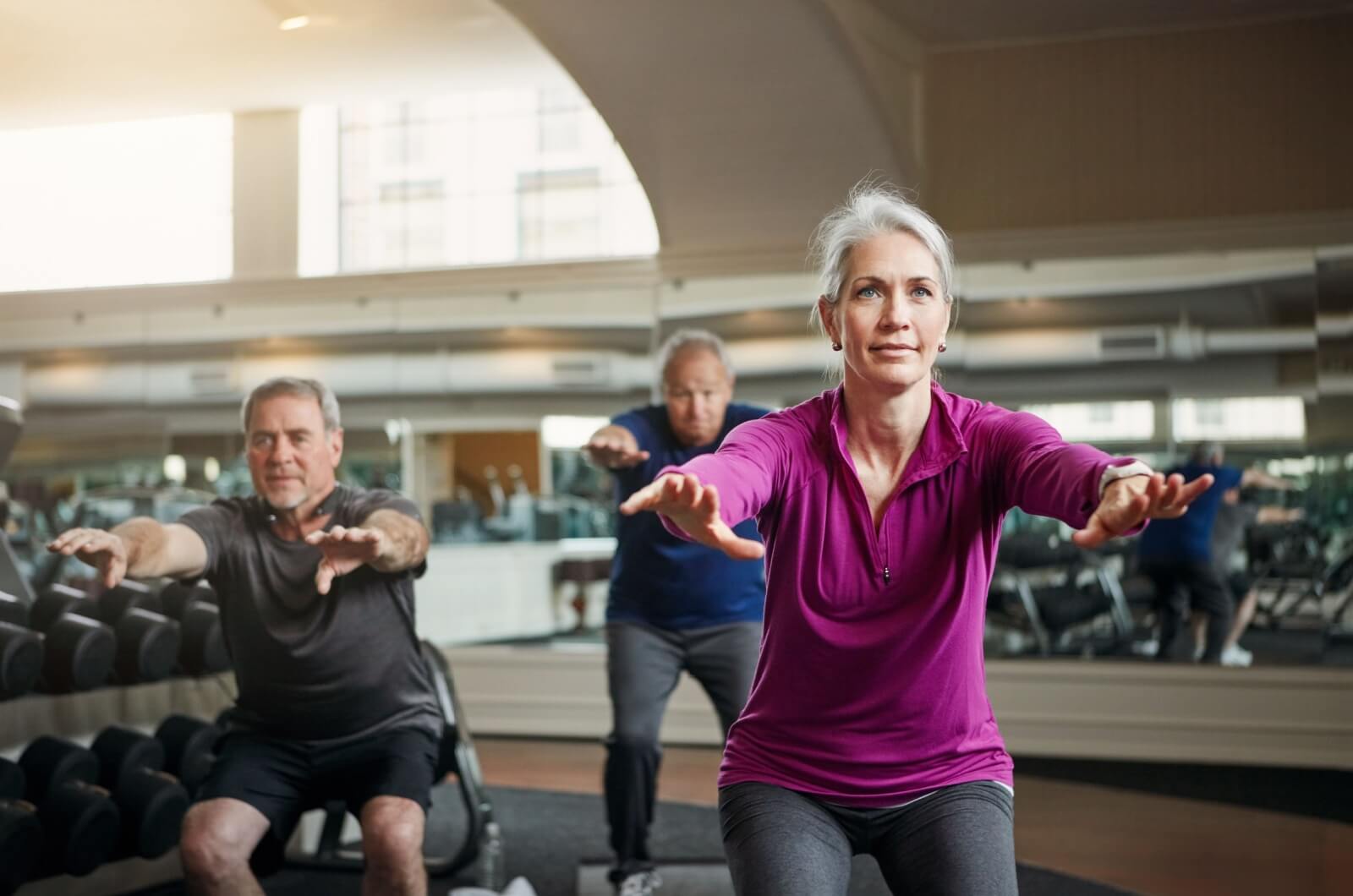 A group of older adults doing squats in a fitness centre.