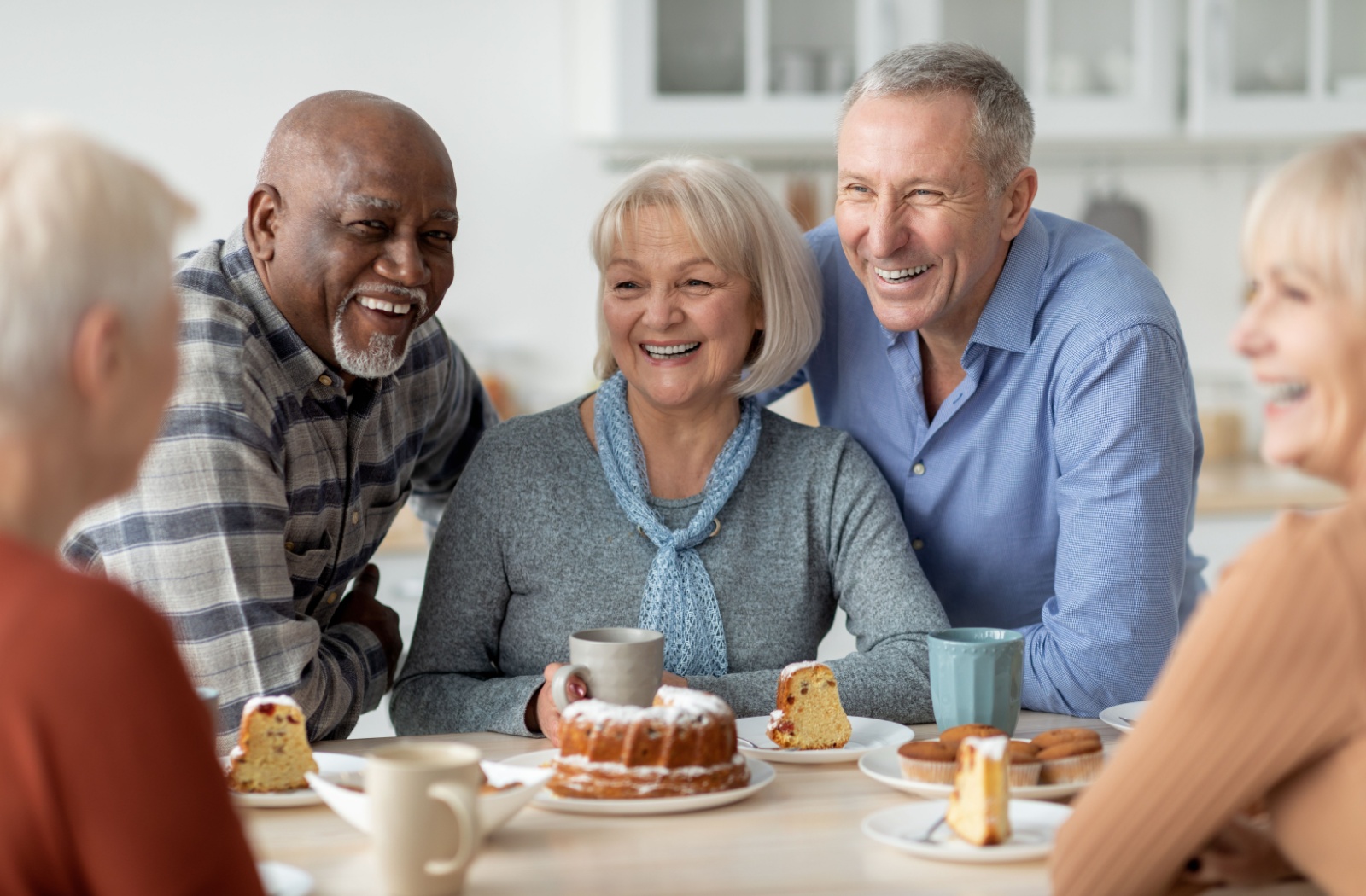 Five older adults sitting around the table with coffee and pastries smiling and laughing in senior living.