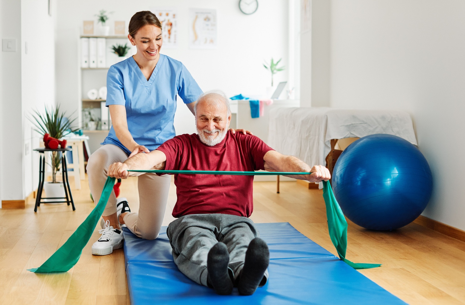 A physical therapist helps a senior perform strengthening exercises with a green resistance band.