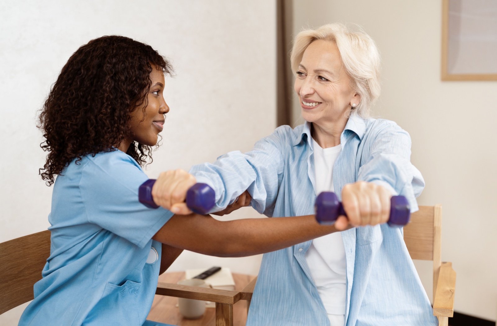 A physical therapist helps a senior with light arm strengthening exercises.
