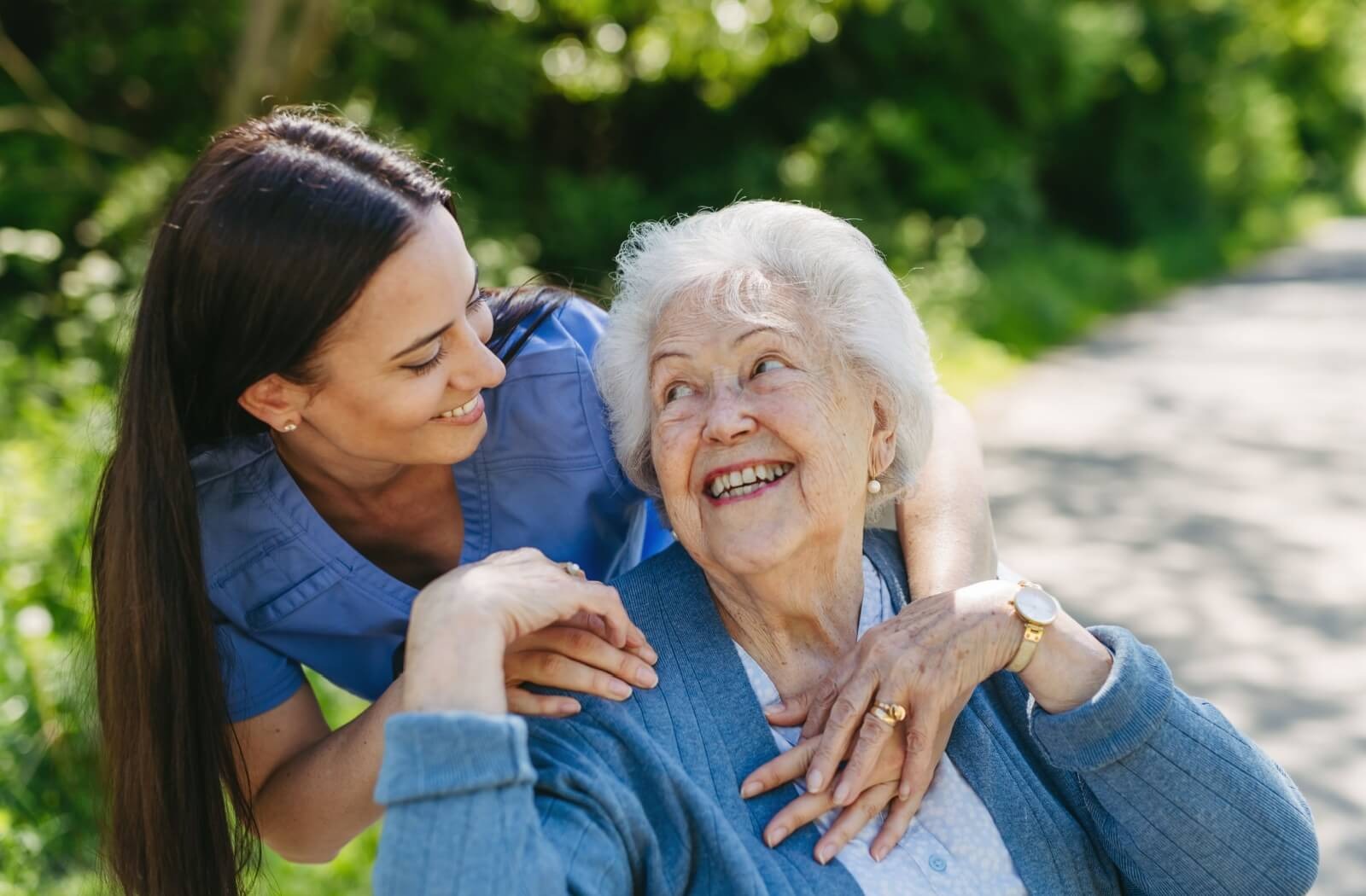 A caregiver surprises a laughing senior from behind while walking in the gardens of an assisted living community
