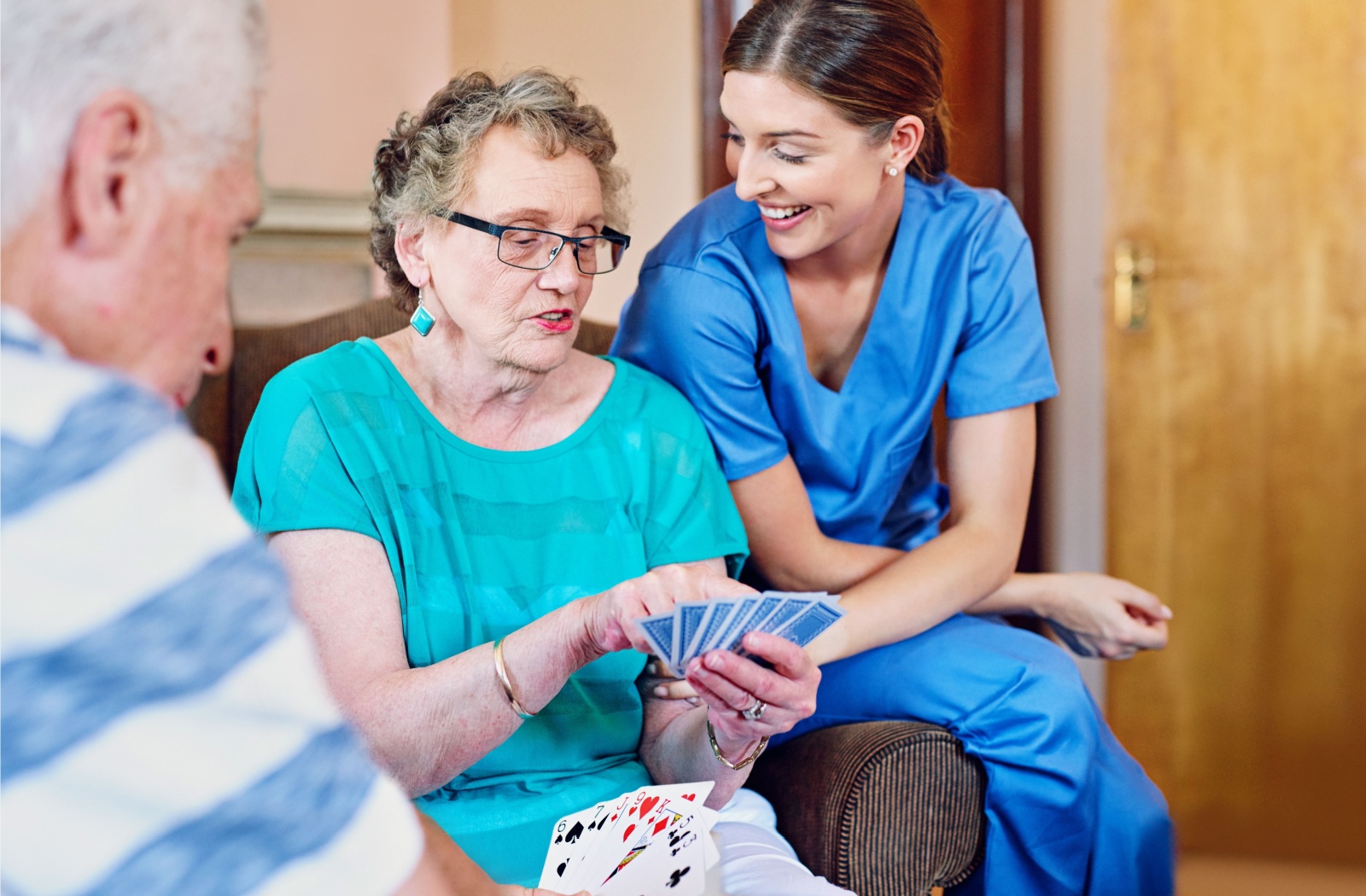 A cheeky resident shows a laughing caregiver their hand of cards while playing a game with another resident in assisted living
