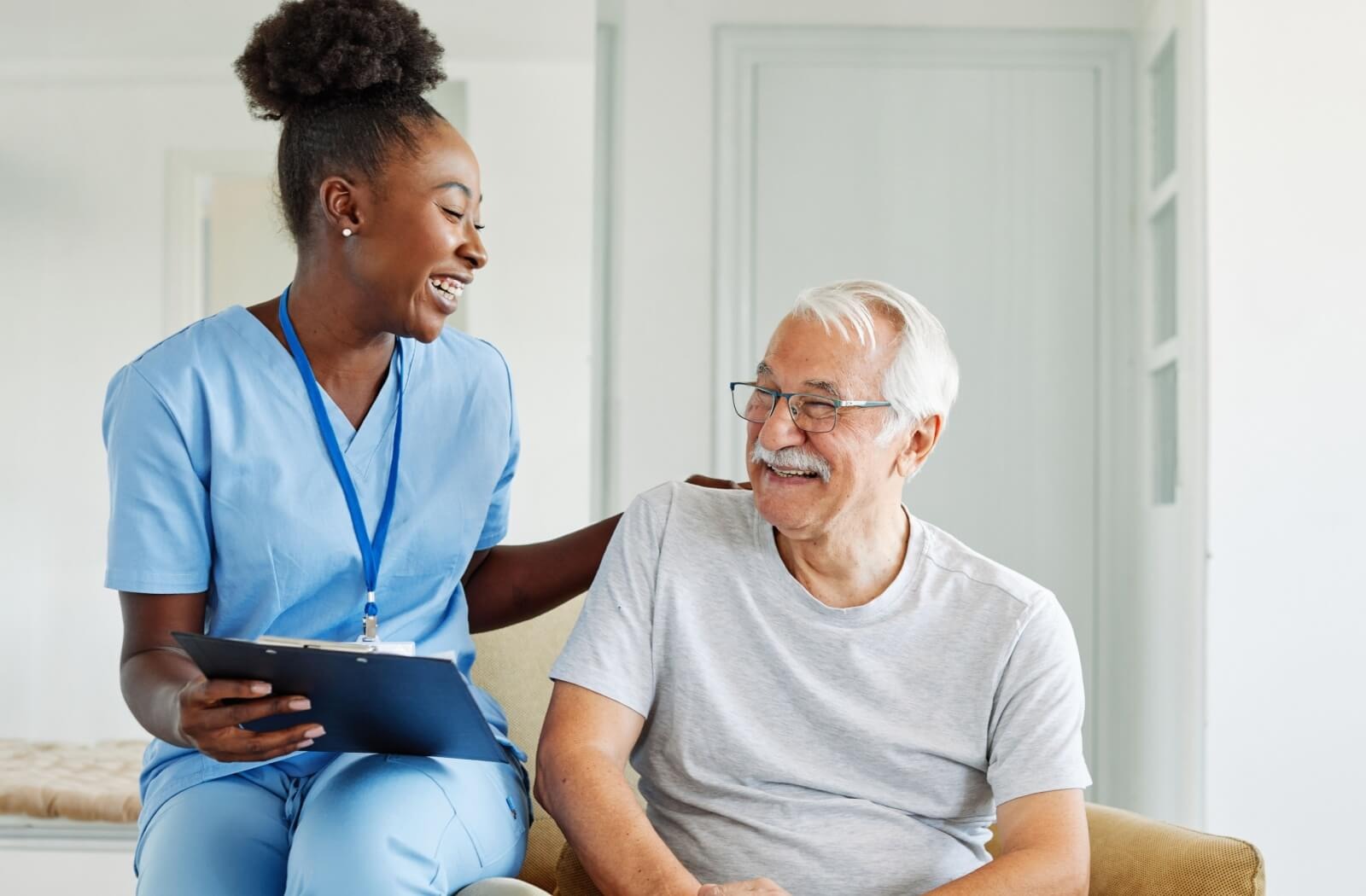 A caregiver holding a clipboard pats the back of a smiling older adult after a memory testing exercise